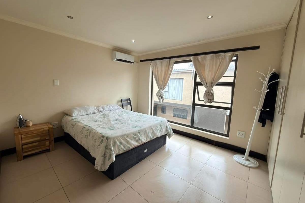 A well-lit bedroom featuring tiled flooring, built-in cupboards, and an integrated air conditioning unit, offering a clean and functional living space.