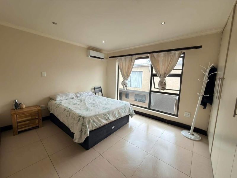 A well-lit bedroom featuring tiled flooring, built-in cupboards, and an integrated air conditioning unit, offering a clean and functional living space.