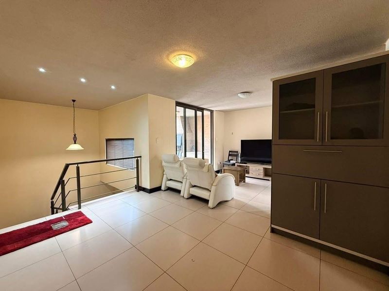 Spacious living area featuring tiled flooring, built-in cabinetry, and a staircase with a modern metal railing, leading to an outdoor balcony area.