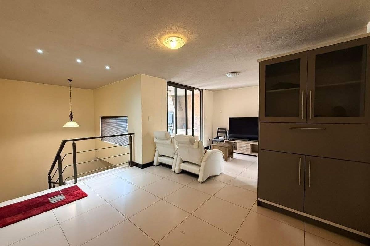 Spacious living area featuring tiled flooring, built-in cabinetry, and a staircase with a modern metal railing, leading to an outdoor balcony area.