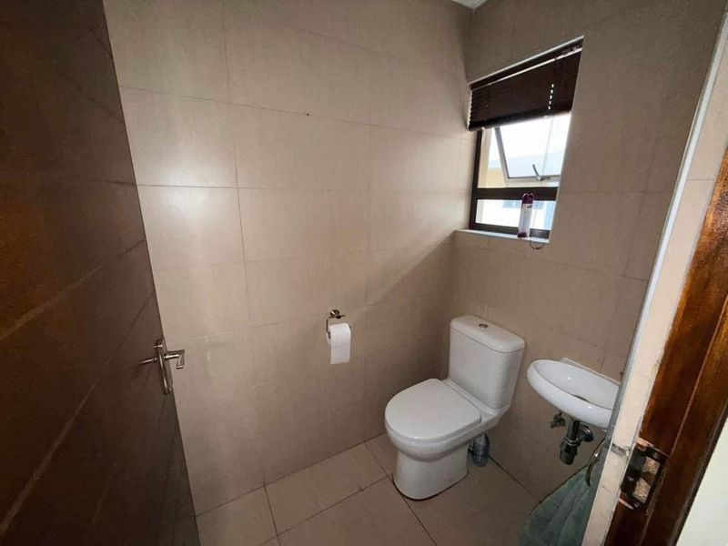 A compact, neutral-toned bathroom featuring a modern toilet, wall-mounted basin, and full-height wall tiling, providing a clean and functional space.