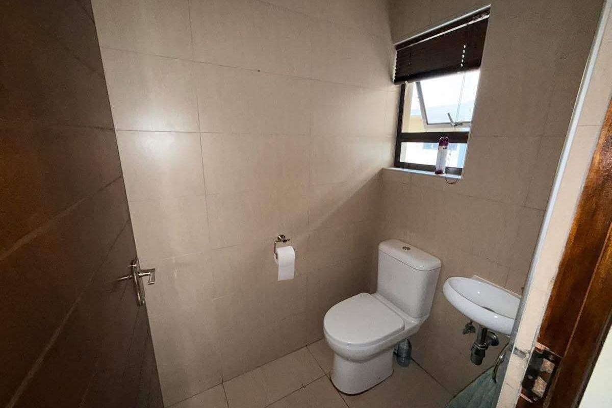 A compact, neutral-toned bathroom featuring a modern toilet, wall-mounted basin, and full-height wall tiling, providing a clean and functional space.