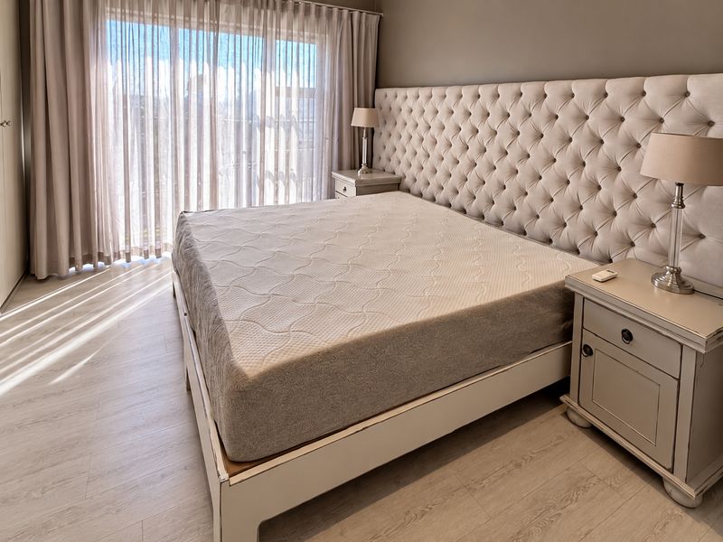 A well-maintained bedroom featuring light-toned laminate flooring and floor-to-ceiling sheer curtains that allow for ample natural light.