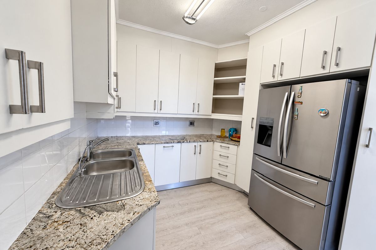 A functional kitchen featuring white cabinetry, granite countertops, a double bowl stainless steel sink, and a tiled backsplash.