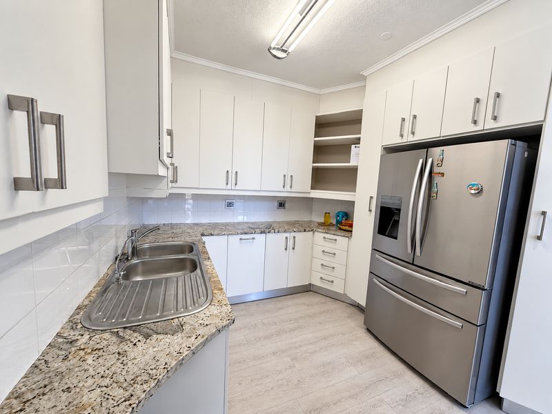 A functional kitchen featuring white cabinetry, granite countertops, a double bowl stainless steel sink, and a tiled backsplash.