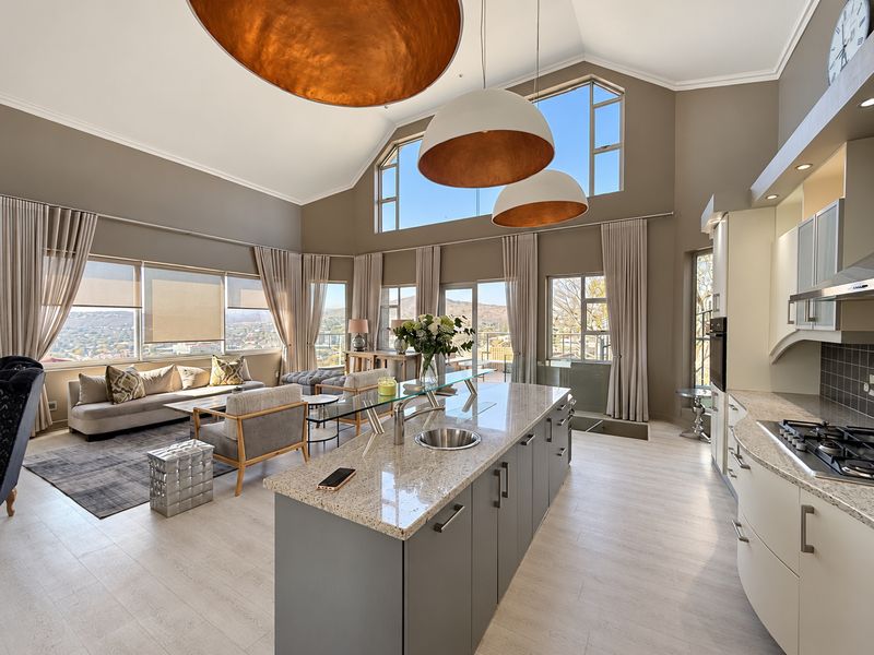 Spacious open-plan living area featuring a modern kitchen with granite island, vaulted ceilings, and expansive windows offering panoramic views.