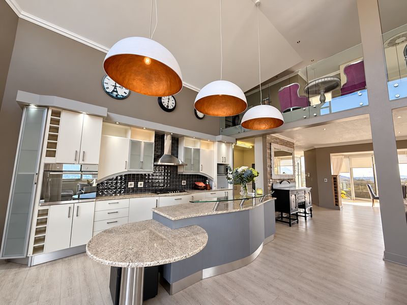 Spacious open-plan kitchen featuring a modern island, granite countertops, high-end built-in appliances, and a mezzanine level with glass balustrades.