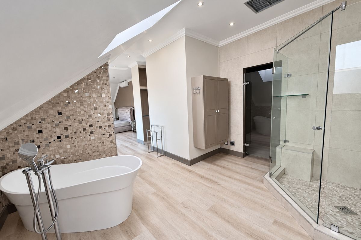 Modern bathroom featuring a freestanding bathtub, glass-enclosed shower, mosaic tile accents, and skylight, offering a bright and contemporary space.