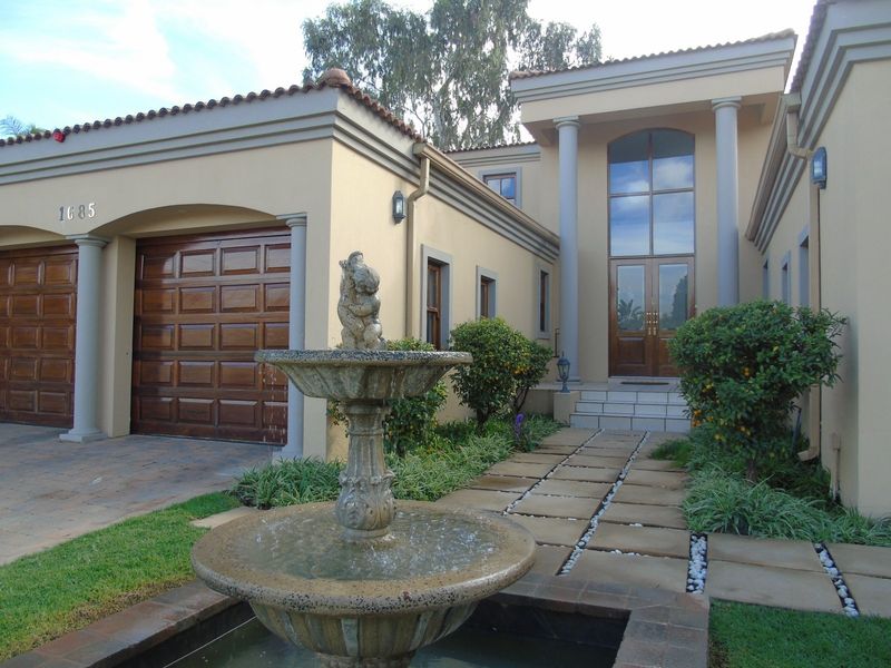 A well-maintained front facade featuring a double garage, grand entrance with columns, and a decorative stone fountain set within a landscaped garden.