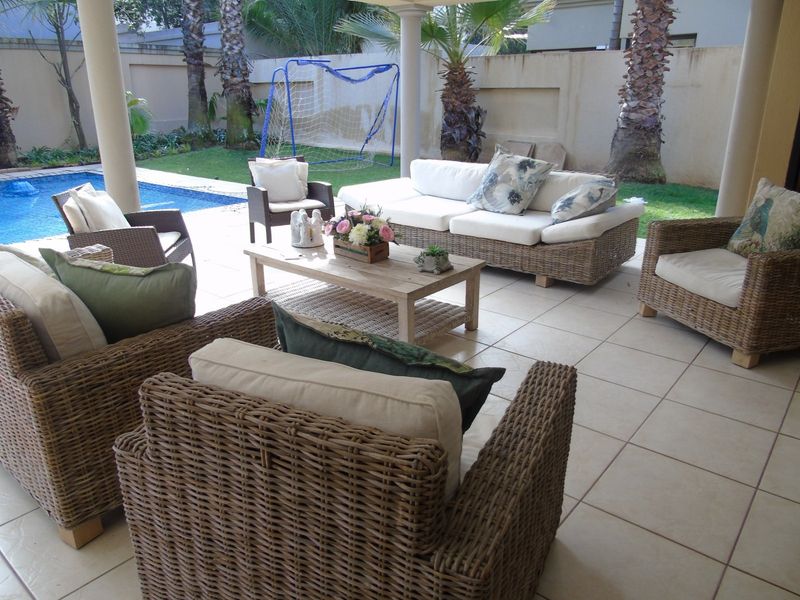 A covered outdoor patio area featuring tiled flooring and structural columns, overlooking a private swimming pool and garden space.