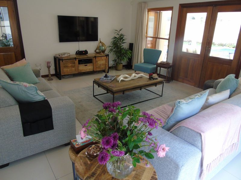 A comfortable living room featuring light-colored tiled flooring and timber-framed glass doors that provide natural light and access to the outdoor area.