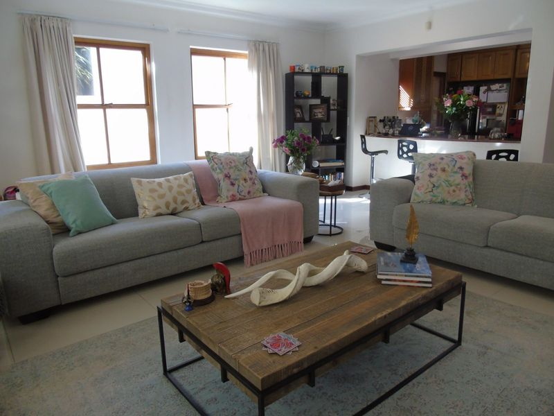 Open-plan living area featuring tiled floors, natural light from wooden-framed windows, and a connected kitchen with a breakfast bar.