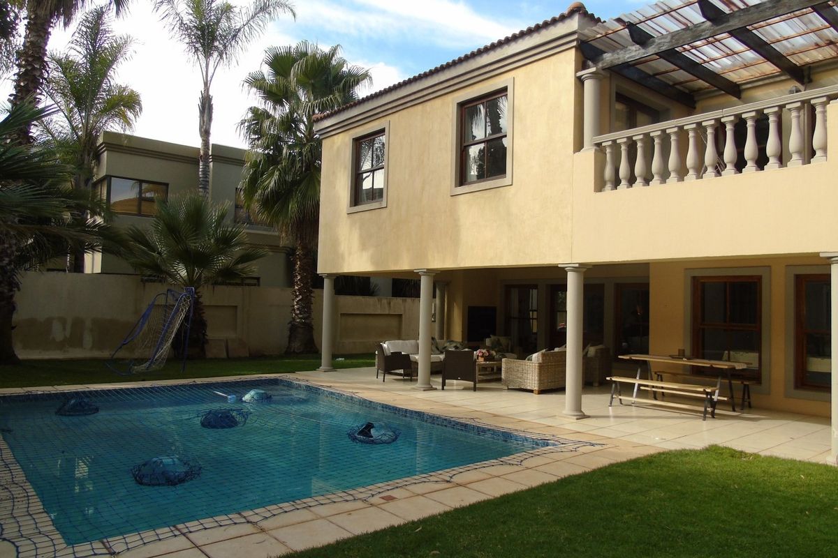 Rear view of the house featuring a swimming pool, a covered patio area, and an upper-level balcony with a balustrade.