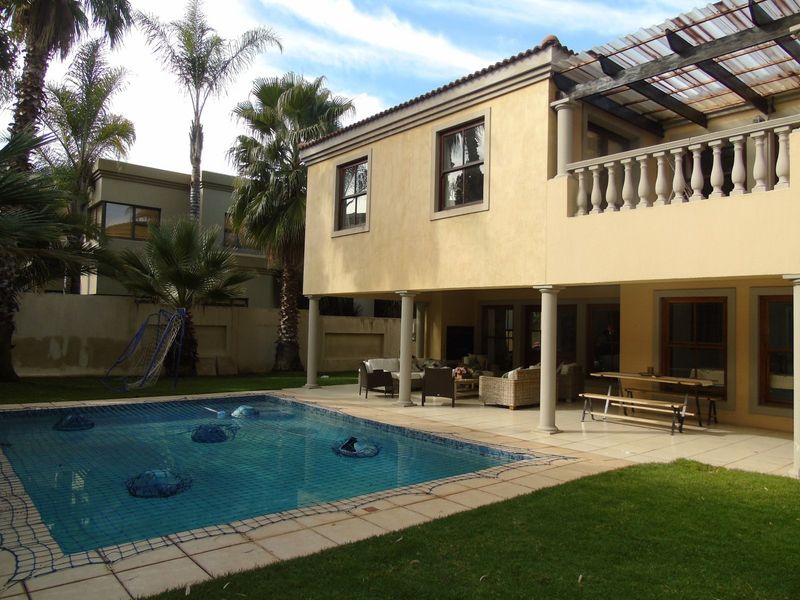 Rear view of the house featuring a swimming pool, a covered patio area, and an upper-level balcony with a balustrade.
