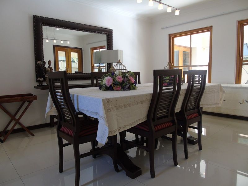 A bright dining room featuring polished tiled flooring, wooden window frames, and modern track lighting, providing a clean and functional space for meals.