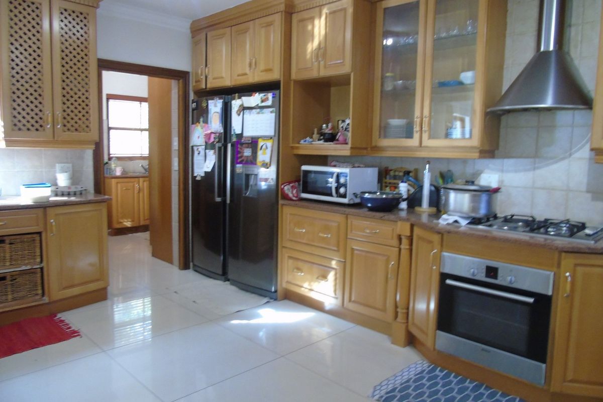A functional kitchen featuring traditional wooden cabinetry, built-in oven, gas hob, stainless steel extractor fan, and tiled flooring with a connecting scullery area.