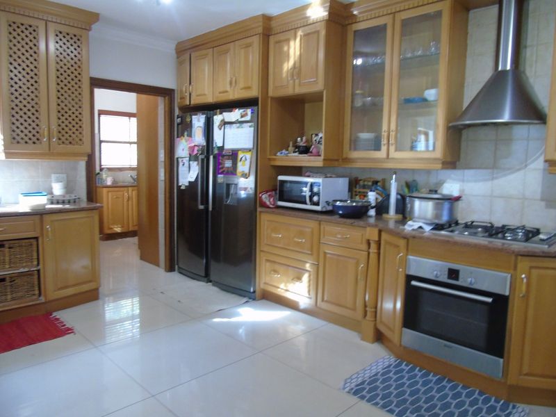 A functional kitchen featuring traditional wooden cabinetry, built-in oven, gas hob, stainless steel extractor fan, and tiled flooring with a connecting scullery area.