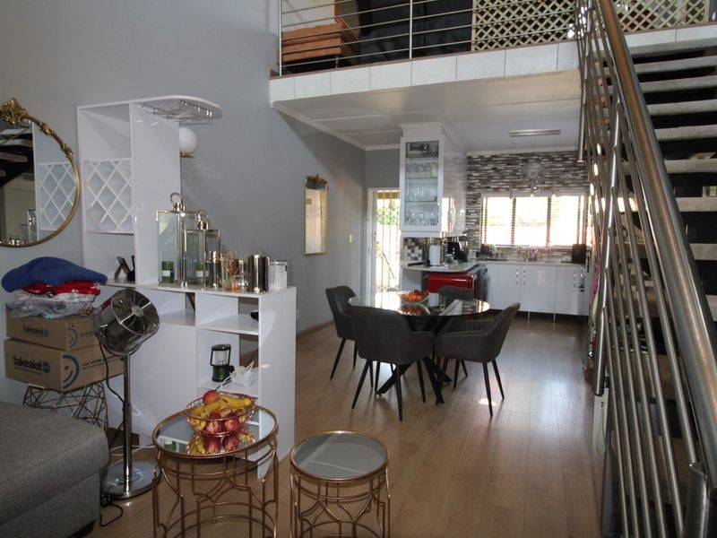 Open-plan living and kitchen area featuring laminate flooring, a modern staircase with metal balustrades, and a mezzanine level overlooking the ground floor.