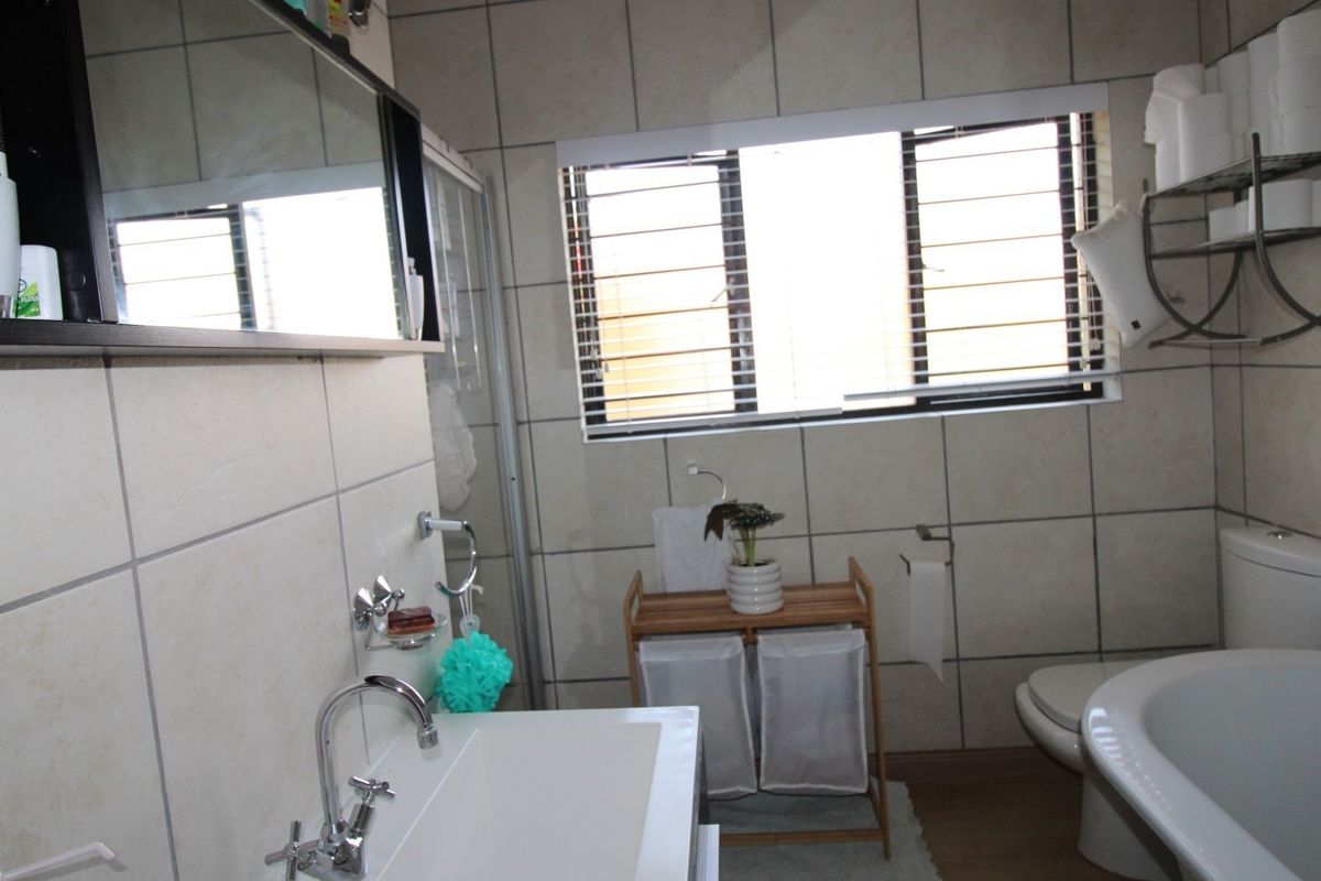 A functional bathroom featuring tiled walls, a wall-mounted vanity basin, a freestanding bathtub, and a separate shower enclosure with natural light from the window.