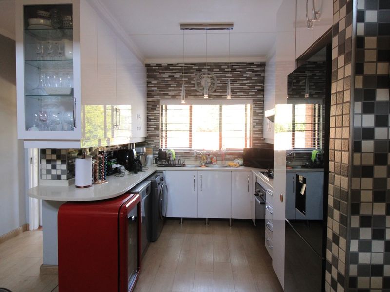 Modern galley-style kitchen featuring white high-gloss cabinetry, stone countertops, mosaic tile backsplash, and integrated appliances with warm laminate flooring.