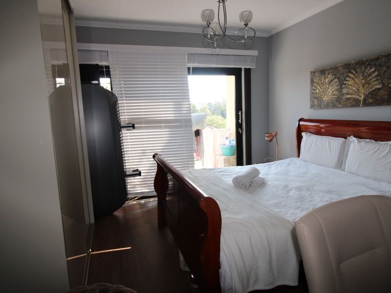 A well-maintained bedroom featuring laminate flooring, built-in cupboards, and a sliding door providing access to an outdoor area with venetian blinds.