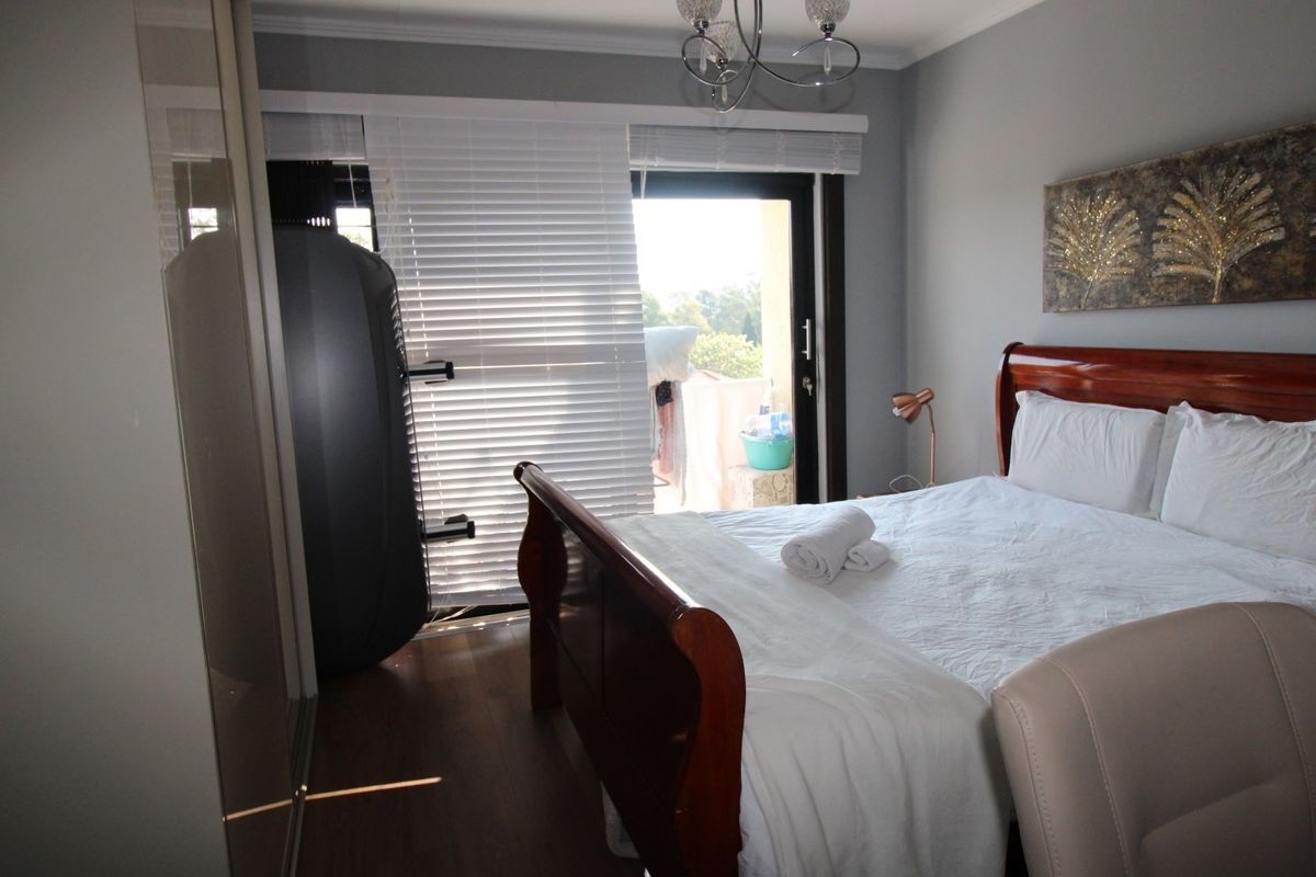 A well-maintained bedroom featuring laminate flooring, built-in cupboards, and a sliding door providing access to an outdoor area with venetian blinds.