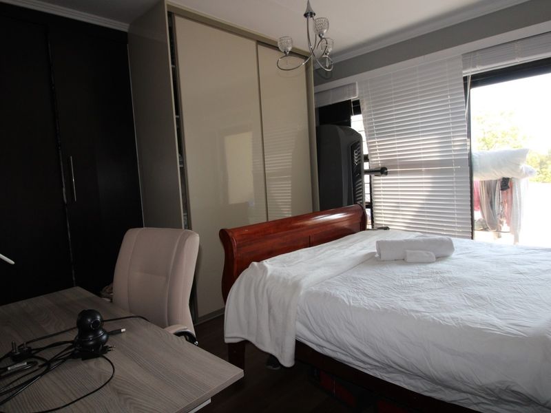 A well-lit bedroom featuring built-in cupboards, laminate flooring, and a sliding door leading to an outdoor area with venetian blinds.