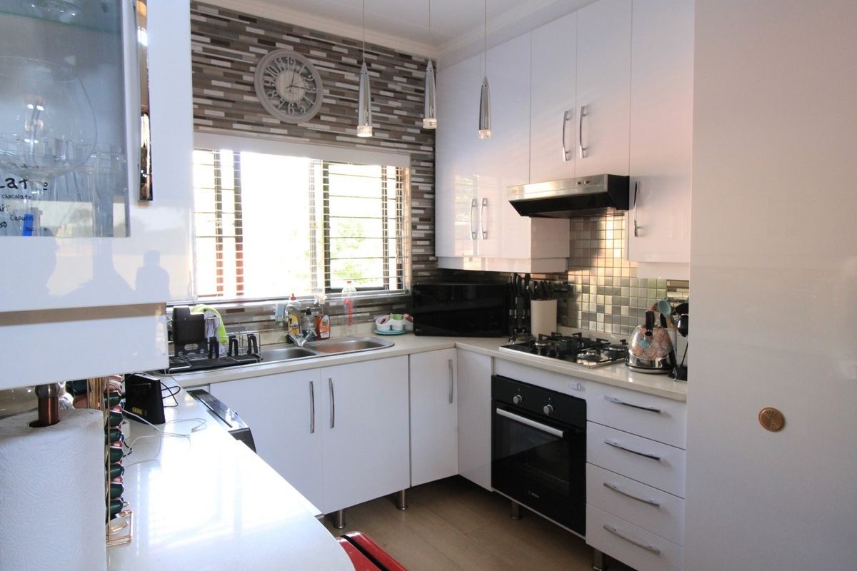 Modern kitchen featuring white high-gloss cabinetry, stone countertops, integrated gas hob, built-in oven, and a decorative tiled splashback.