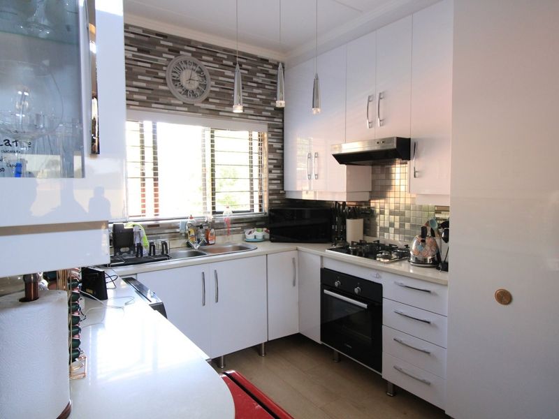 Modern kitchen featuring white high-gloss cabinetry, stone countertops, integrated gas hob, built-in oven, and a decorative tiled splashback.