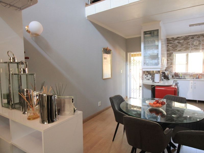 Open-plan living and dining area featuring laminate flooring, a mezzanine level, and a functional kitchen with built-in cabinetry and mosaic tile backsplash.