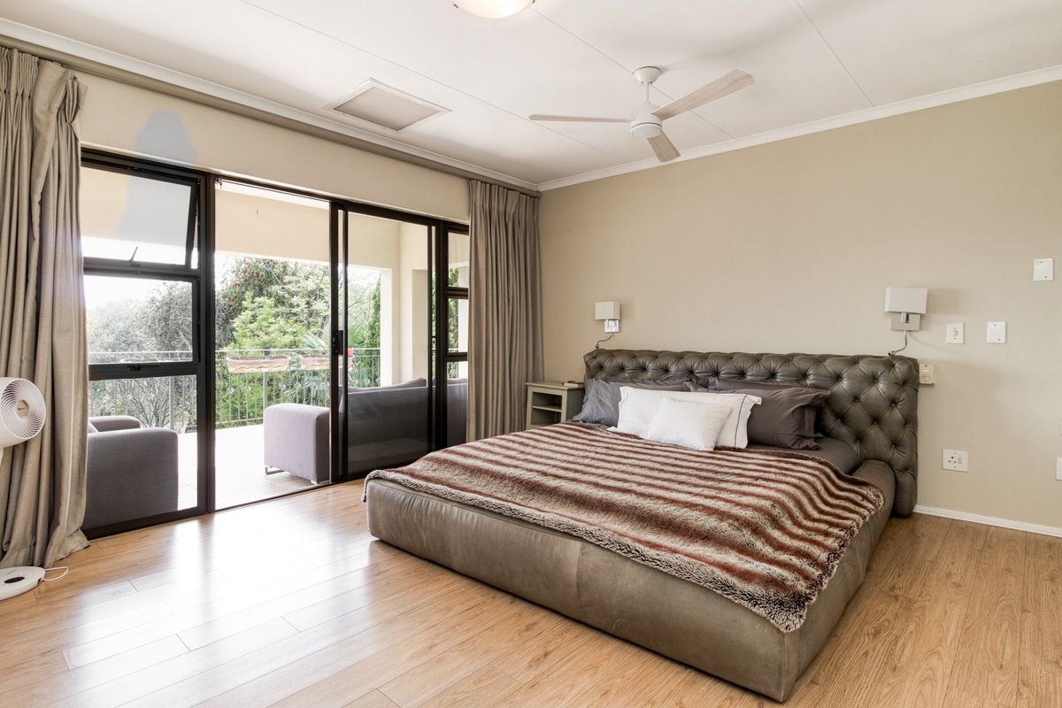 Spacious bedroom featuring light wood-look flooring, a ceiling fan, and large sliding glass doors opening onto a private balcony.