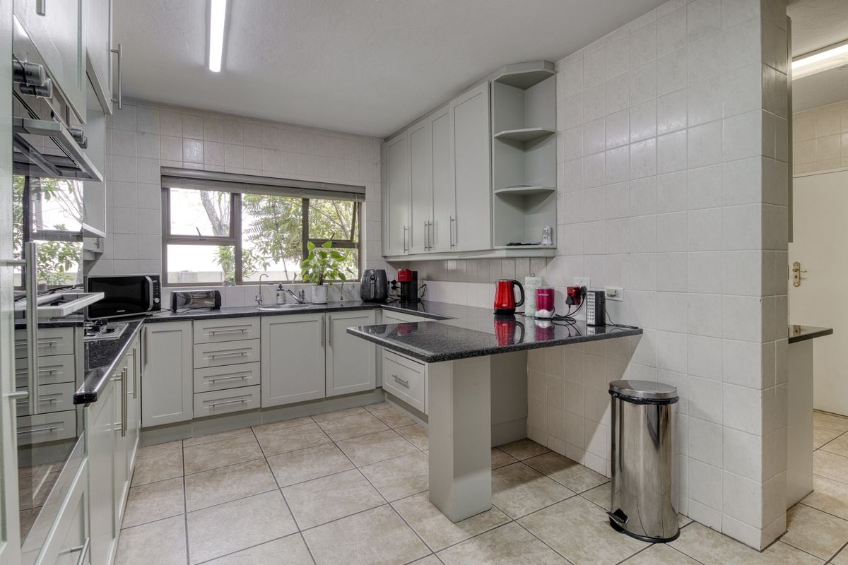 Functional kitchen featuring light grey cabinetry, granite countertops, a breakfast bar, built-in oven, and tiled flooring with a window overlooking the garden.