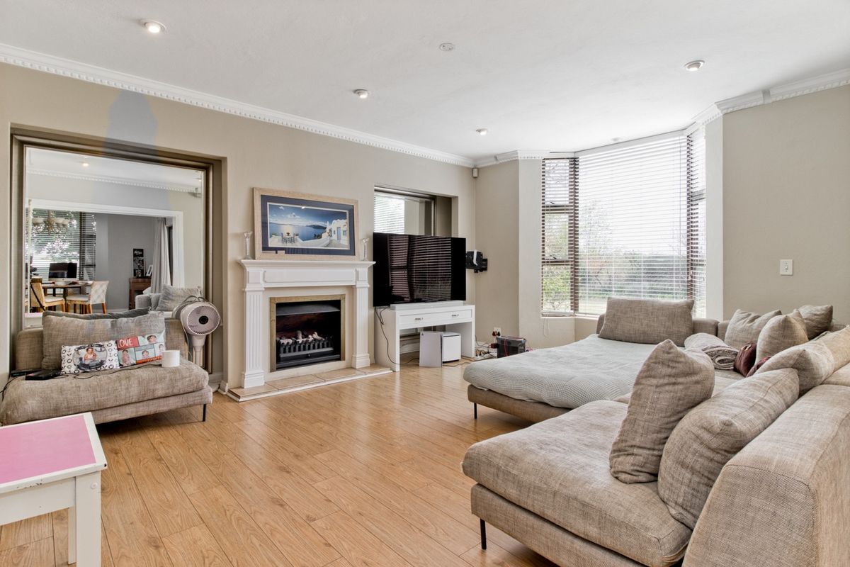 Spacious living room featuring light wood-look flooring, a classic fireplace with mantel, crown molding, and a large bay window allowing for ample natural light.