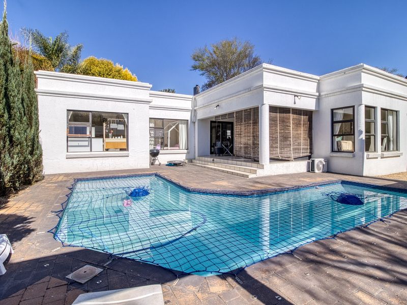 Rear exterior view featuring a swimming pool with safety net, paved patio area, and covered outdoor space attached to the main residence.