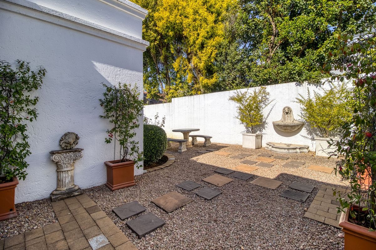 A well-maintained rear courtyard featuring gravel landscaping, stone pavers, and a decorative wall fountain against a white boundary wall.