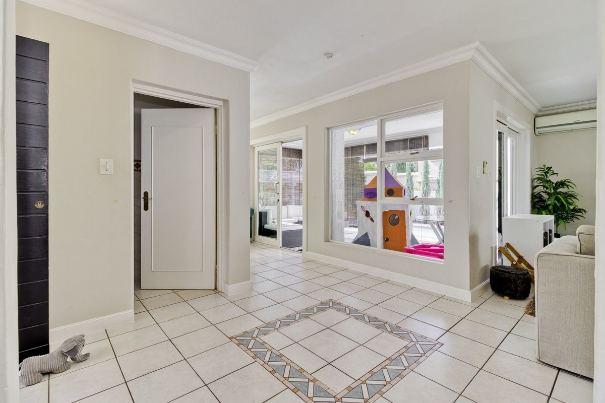 Bright living area featuring tiled flooring with decorative inlay, crown molding, and large windows providing natural light and views to the outdoor patio area.