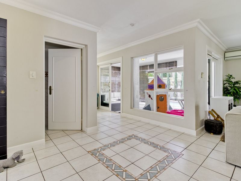 Bright living area featuring tiled flooring with decorative inlay, crown molding, and large windows providing natural light and views to the outdoor patio area.