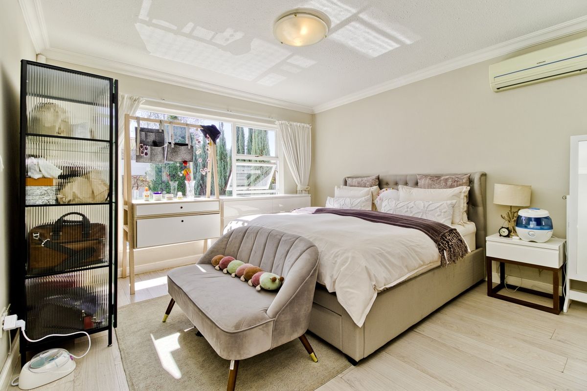 A well-lit bedroom featuring laminate flooring, a split-system air conditioner, and classic cornice detailing, offering a comfortable and functional living space.