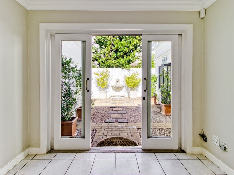 A bright interior view looking out through double glass doors onto a private courtyard featuring a decorative wall fountain and gravel landscaping.