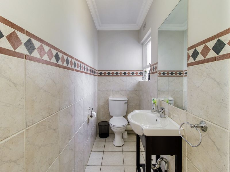 A compact guest bathroom featuring a pedestal washbasin, toilet, and decorative ceramic wall tiling with a neutral finish.