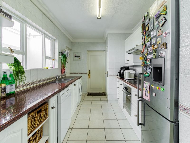 A functional galley-style kitchen featuring granite countertops, white cabinetry, built-in oven, extractor fan, and tiled finishes throughout.