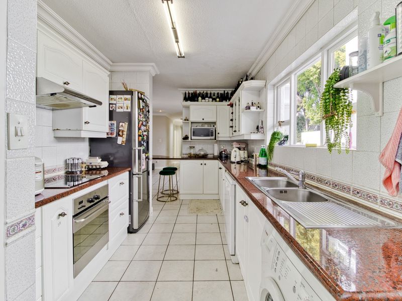 A functional galley-style kitchen featuring granite countertops, built-in cabinetry, an electric hob, oven, and a double basin sink with tiled finishes.