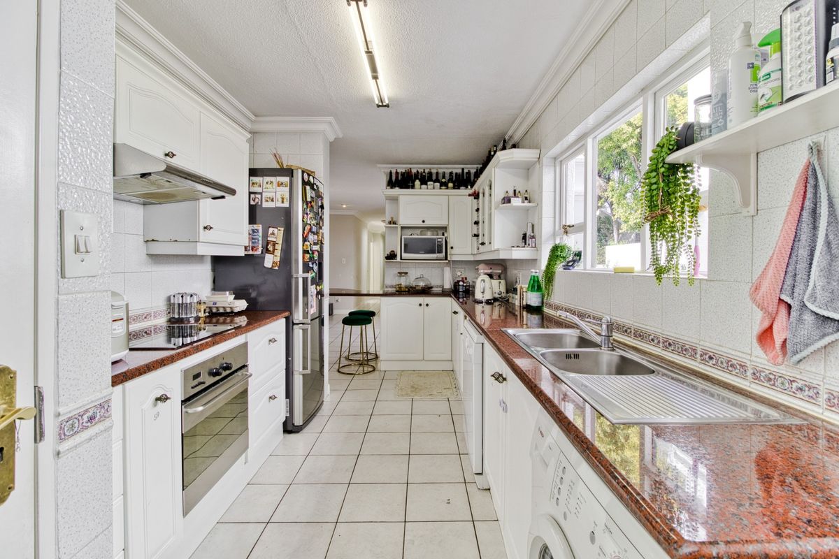 A functional galley-style kitchen featuring granite countertops, built-in cabinetry, an electric hob, oven, and a double basin sink with tiled finishes.