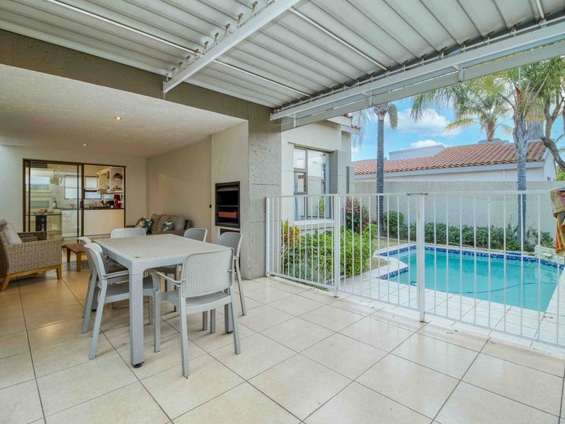 Covered patio area featuring a built-in braai, tiled flooring, and direct access to a private swimming pool with safety fencing.