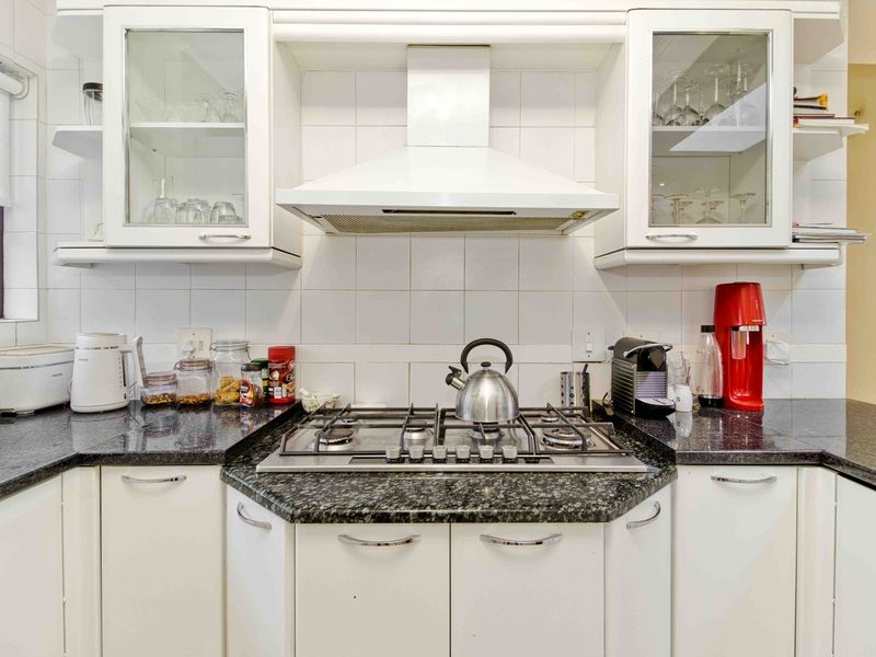 A functional kitchen featuring white cabinetry, granite countertops, a gas hob, and an integrated extractor fan with a tiled backsplash.