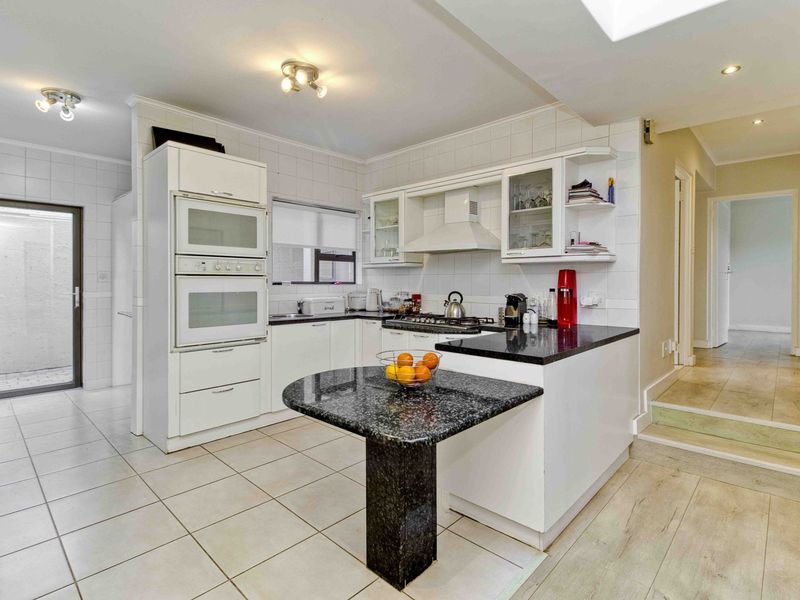 A functional kitchen featuring white cabinetry, granite countertops, a built-in double oven, gas hob, and tiled flooring with direct access to an outdoor area.