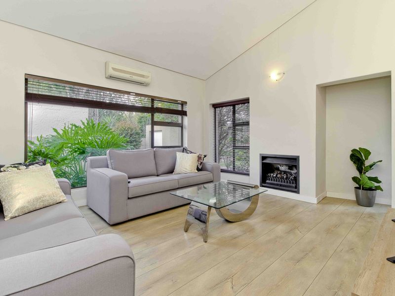 A bright living room featuring laminate flooring, a built-in fireplace, a wall-mounted air conditioner, and large windows overlooking the garden.