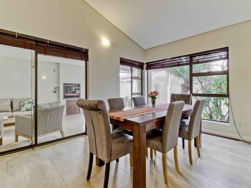 Bright dining area featuring laminate flooring, vaulted ceilings, and large windows with direct access to a covered patio through sliding glass doors.