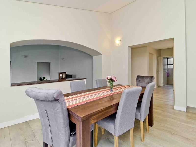 A bright dining area featuring light laminate flooring, high ceilings, and a distinctive arched wall opening connecting to the adjacent space.