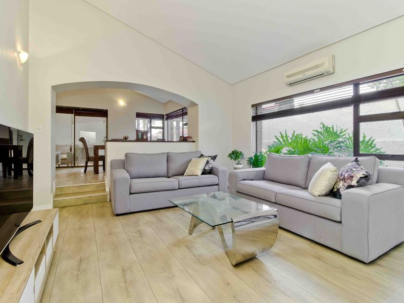 A bright and spacious living room featuring laminate flooring, a split-system air conditioner, and an archway leading to an adjacent dining area.